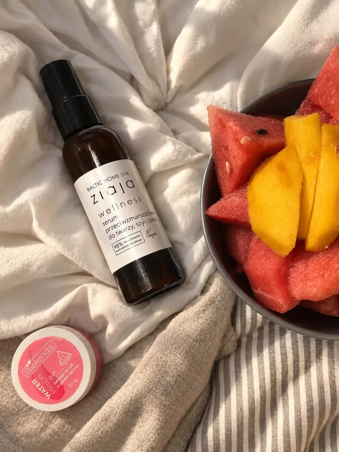 Serum Ziaja Baltic Home Spa Wellness i balsam do ust Bielenda Watermelon obok arbuza i mango na jasnej tkaninie